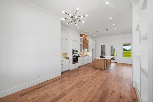 a large white kitchen with wooden floor and a chandelier