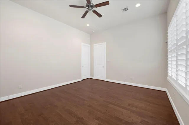 an empty room with wooden floor fan and windows