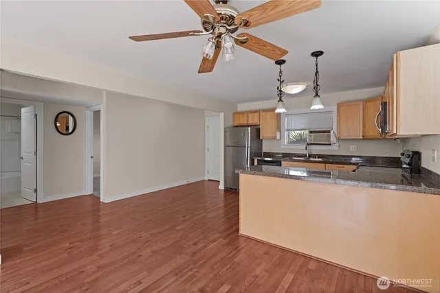 a large kitchen with stainless steel appliances granite countertop a sink a stove a refrigerator and white cabinets with wooden floor