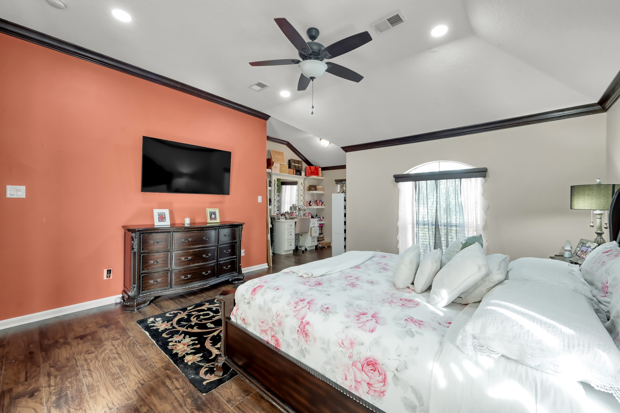 1000 Arbor Way Conroe, TX 77303 - Photo 15 of 29 This spacious bedroom features a vaulted ceiling with recessed lighting and a ceiling fan. It has a warm accent wall, luxury vinyl plan floors, and a large window for natural light and an adjoining area offers extra space, possibly for a home office or vanity area.