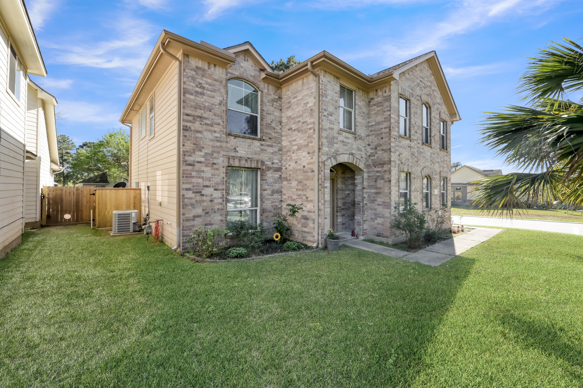 1000 Arbor Way Conroe, TX 77303 - Photo 2 of 29 Two-story brick home with a well-maintained lawn and a small garden near the entrance. The property includes a side yard with a wooden fence and an outdoor AC unit. The house features multiple windows, allowing for ample natural light.
