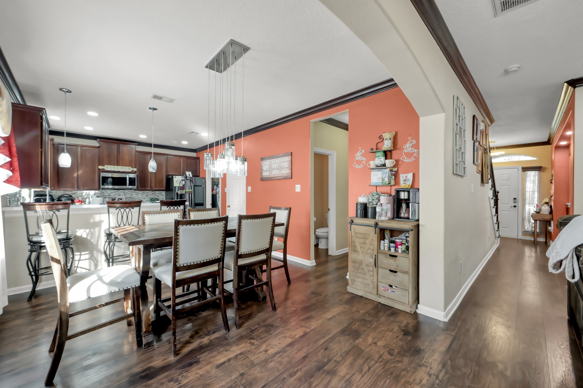 1000 Arbor Way Conroe, TX 77303 - Photo 9 of 29 Enojoy the open-concept dining area and kitchen with luxury vinyl plan floors throughout and a vibrant accent wall. The kitchen features dark wood cabinetry, modern pendant lighting, and a breakfast bar. The space is bright and inviting, ideal for family gatherings and entertaining. Refrigerator NOT included.