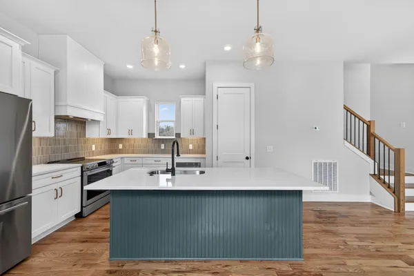 a kitchen with stainless steel appliances granite countertop a sink a stove a refrigerator cabinets and a wooden floor