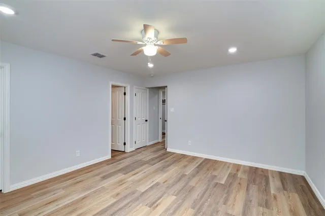 a view of an empty room with wooden floor and a fan