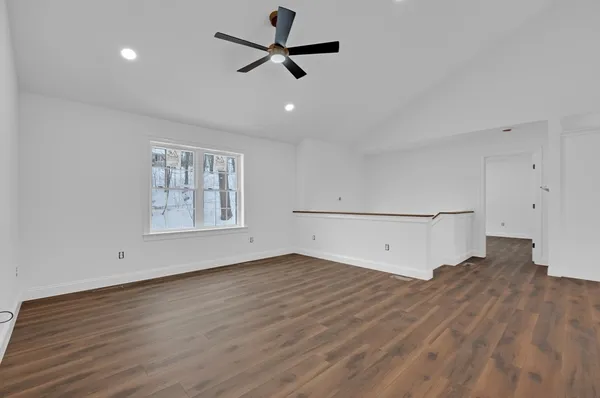 a view of an empty room with wooden floor and a ceiling fan