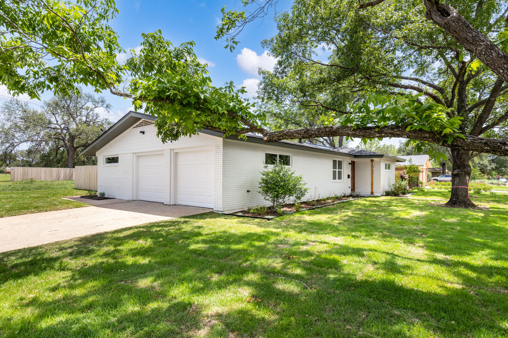 4501 Pack Saddle Pass Austin, TX 78745 - Photo 37 of 37 White brick exterior featuring a dark gray roofline, two garage doors, a concrete driveway, and mature landscaping