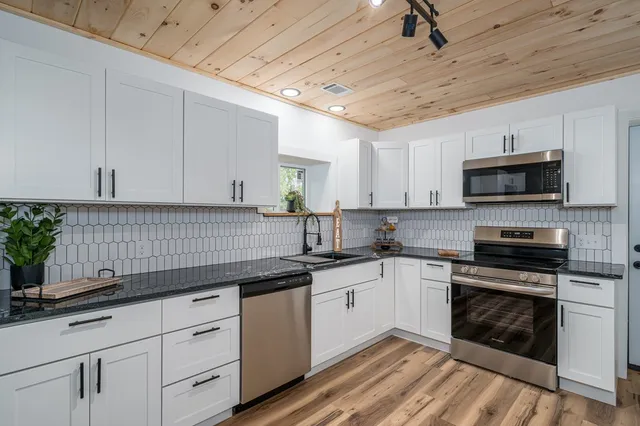 a kitchen with granite countertop a sink stainless steel appliances and white cabinets