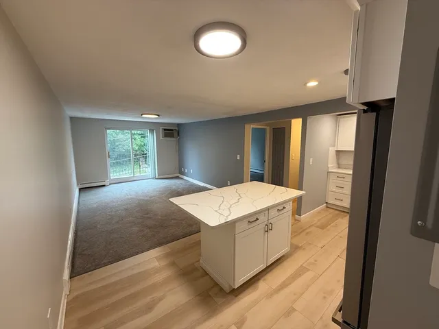 a hall with kitchen island white cabinets and wooden floor