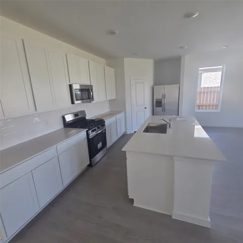 a large white kitchen with cabinets appliances a sink and a window