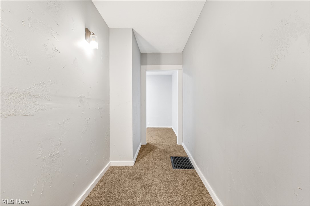 885 Wales Road Northeast Massillon, OH 44646 - Photo 11 of 34 Carpeted hallway featuring white trim, a wall-mounted light fixture, and a floor vent