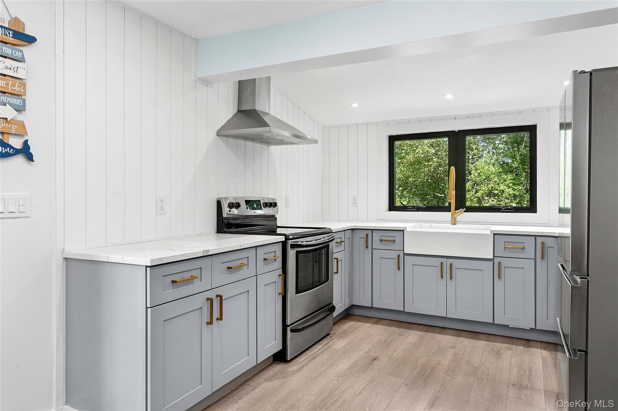 73175 Main Road Greenport, NY 11944 - Photo 5 of 15 Kitchen with gray cabinetry, stainless steel appliances, wall chimney range hood, light wood-style flooring, and recessed lighting