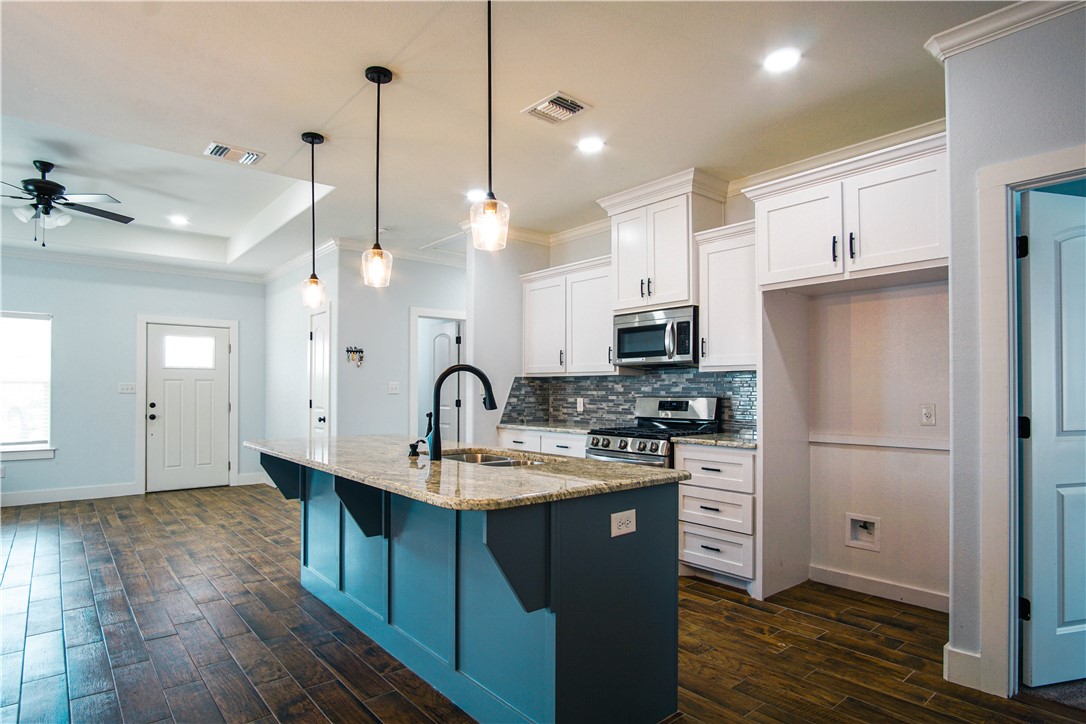 1614 Louis Street Bryan, TX 77803 - Photo 8 of 29 Kitchen featuring white cabinetry, light stone counters, stainless steel appliances, a kitchen island with sink, and hanging light fixtures