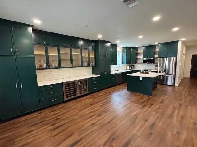 a room with stainless steel appliances kitchen island granite countertop wooden cabinets and a large window