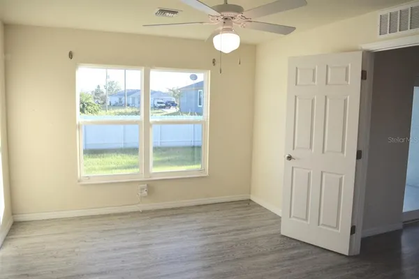 an empty room with wooden floor fan and windows