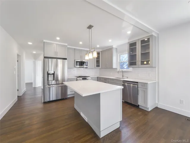 a large kitchen with kitchen island a stove a sink a refrigerator and white cabinets with wooden floor