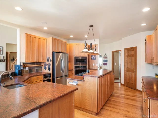 a kitchen with stainless steel appliances granite countertop a refrigerator a stove and a sink with wooden floor