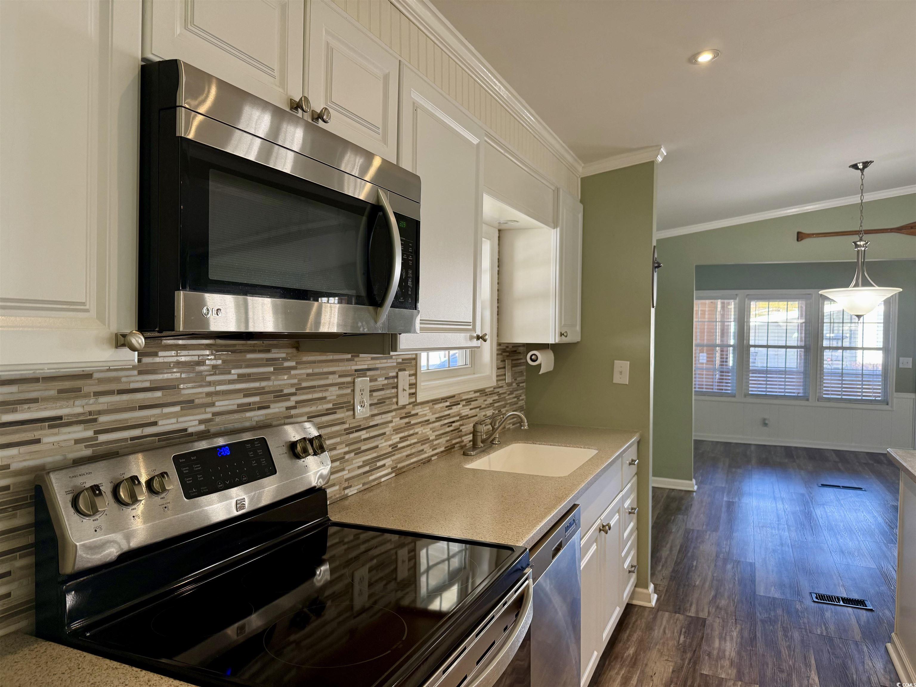 465 Sandpebble Surfside Beach, SC 29575 - Photo 2 of 40 Kitchen featuring stainless steel appliances, white cabinets, dark wood-style floors, crown molding, and light stone countertops