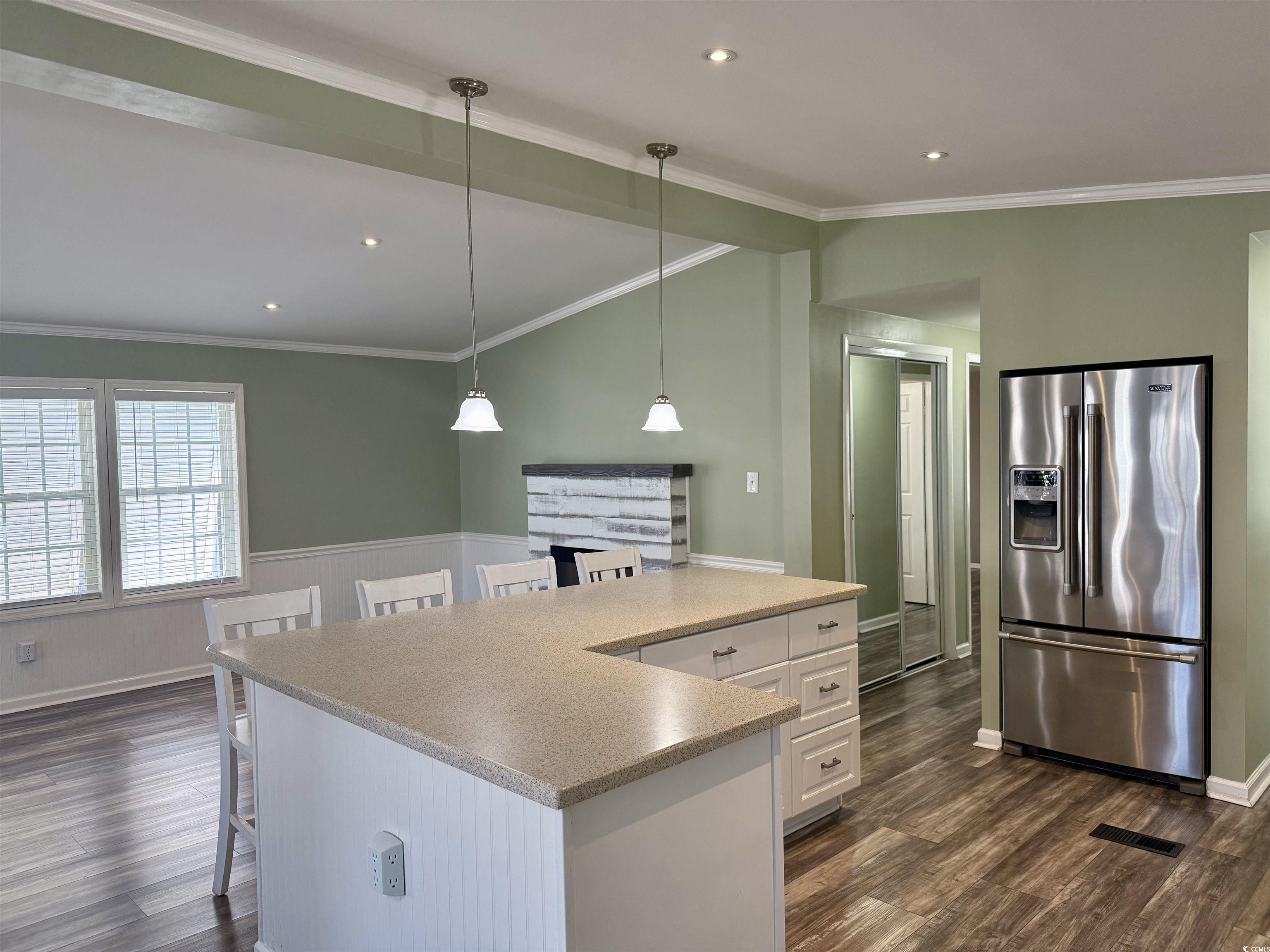 465 Sandpebble Surfside Beach, SC 29575 - Photo 4 of 40 Kitchen with stainless steel fridge with ice dispenser, ornamental molding, a breakfast bar area, dark wood finished floors, and white cabinets