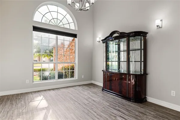 an empty room with wooden floor chandelier and windows