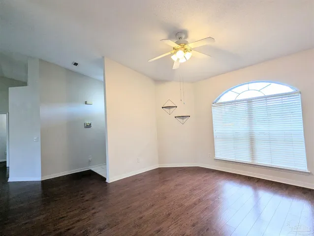 an empty room with wooden floor chandelier fan and windows