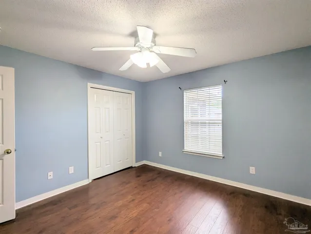 an empty room with wooden floor ceiling fan and windows