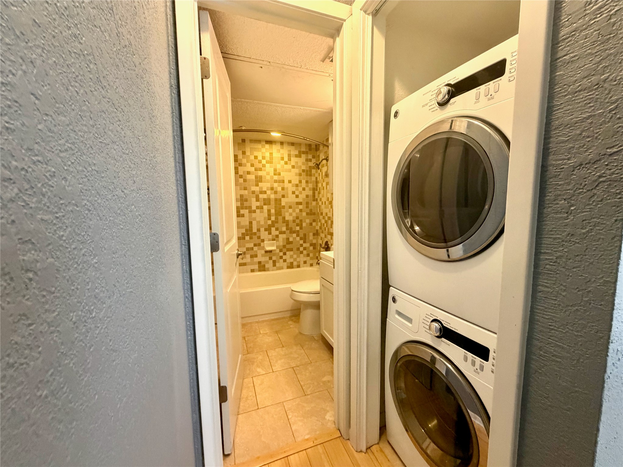 3204 Manchaca Road, Unit 302 Austin, TX 78704 - Photo 11 of 20 A stacked laundry setup sits adjacent to a bathroom featuring custom wall tiling.