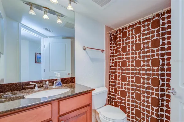 a bathroom with a granite countertop sink a toilet a mirror and shower