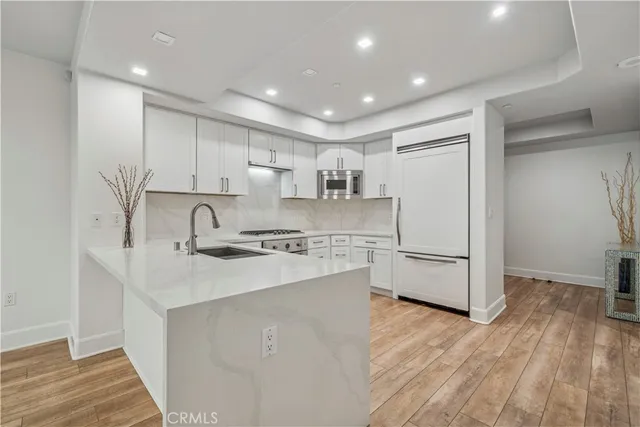 a kitchen with kitchen island a sink a stove a refrigerator and white cabinets with wooden floor