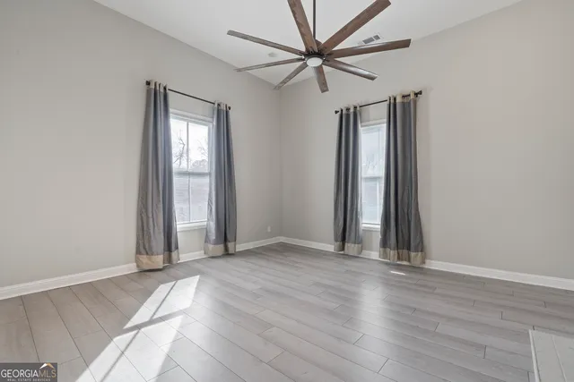 an empty room with wooden floor fan and windows