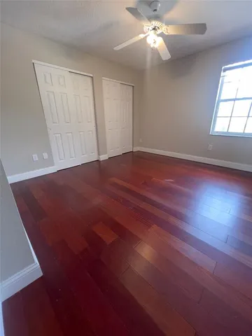 an empty room with wooden floor fan and windows