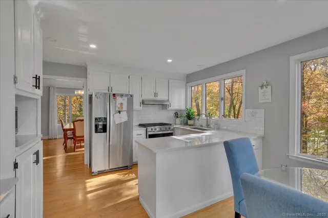 a kitchen with stainless steel appliances granite countertop a refrigerator a stove a sink dishwasher and white cabinets with wooden floor