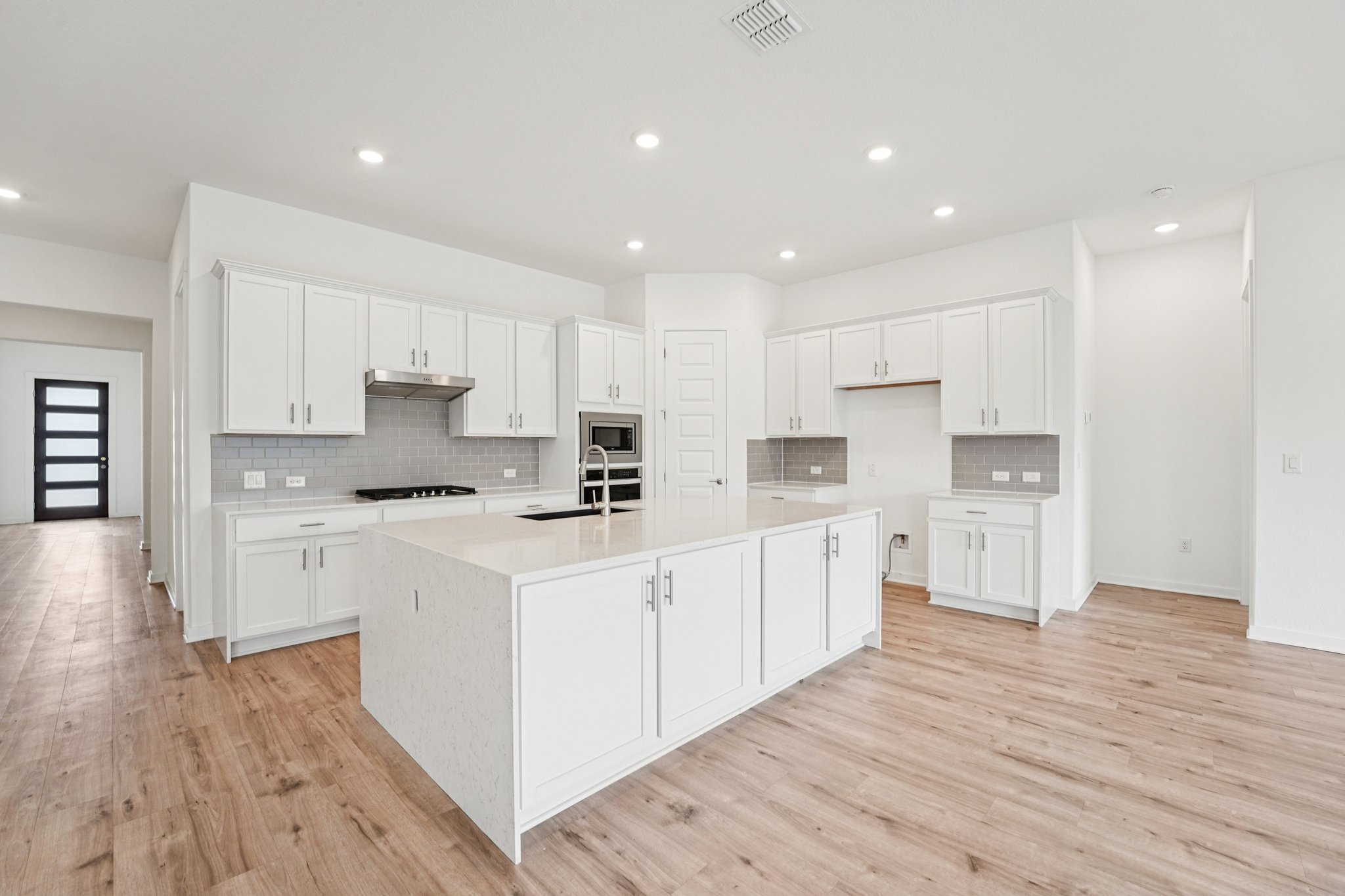 2233 Bravo Pass Leander, TX 78641 - Photo 10 of 33 Kitchen featuring white cabinetry, an island with sink, light stone counters, recessed lighting, and tasteful backsplash