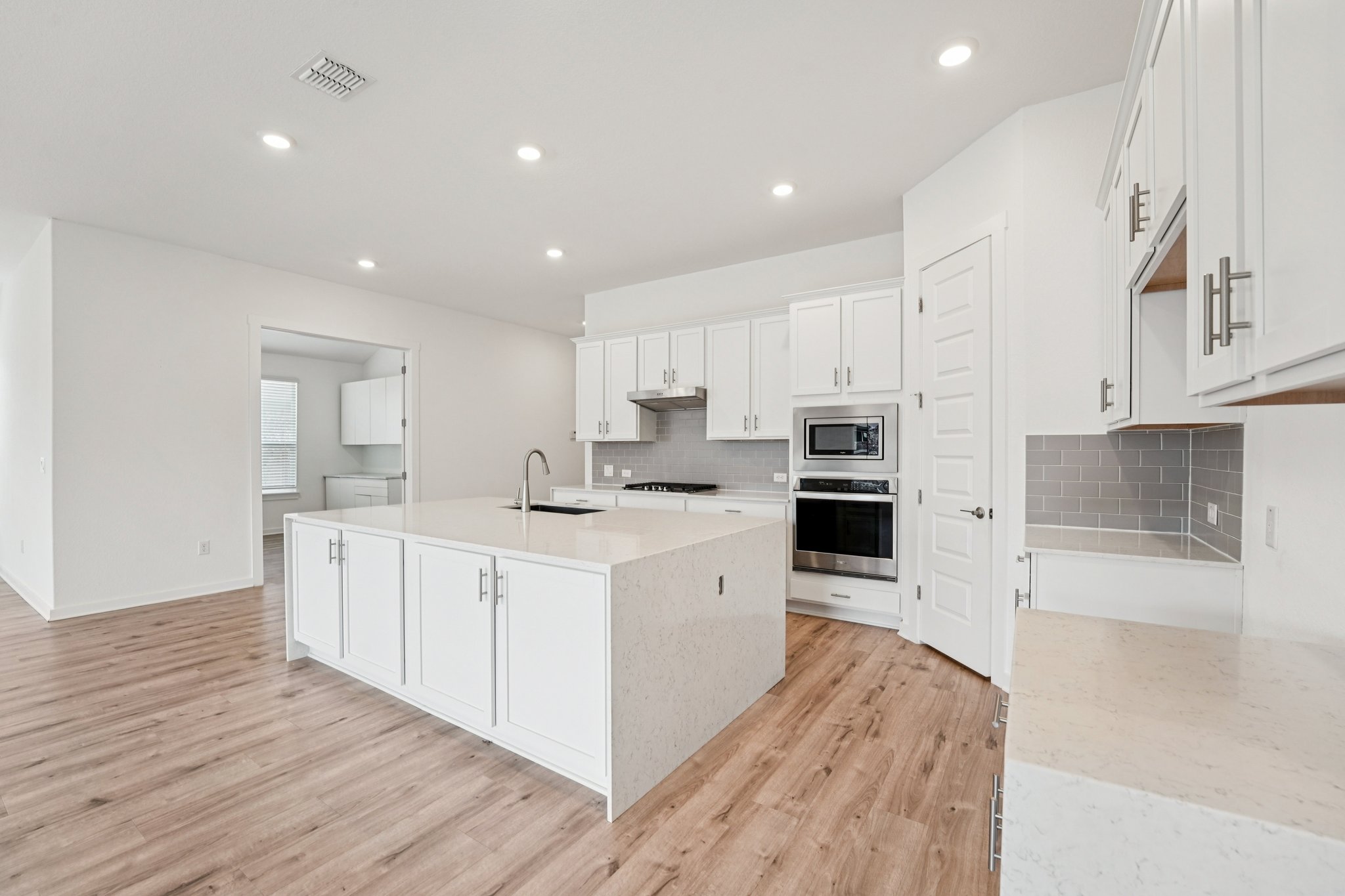 2233 Bravo Pass Leander, TX 78641 - Photo 12 of 33 Kitchen with light stone countertops, a center island with sink, white cabinetry, decorative backsplash, and recessed lighting