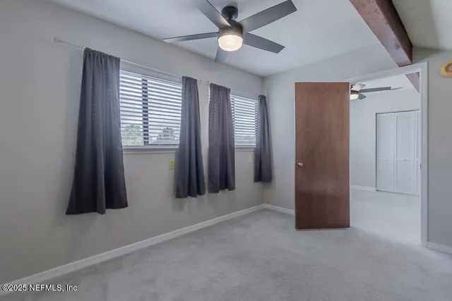 an empty room with chandelier fan and windows