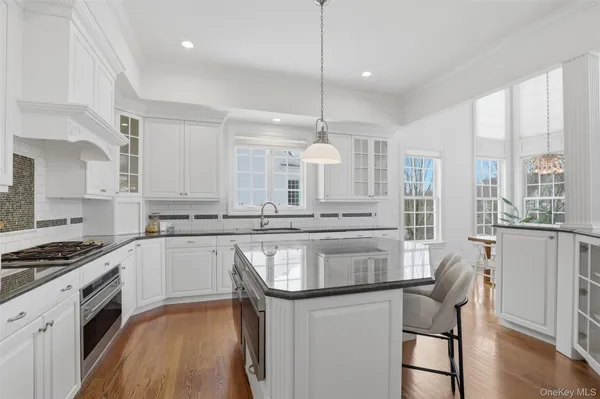 a kitchen with stainless steel appliances granite countertop a stove a sink dishwasher a refrigerator and white cabinets with wooden floor