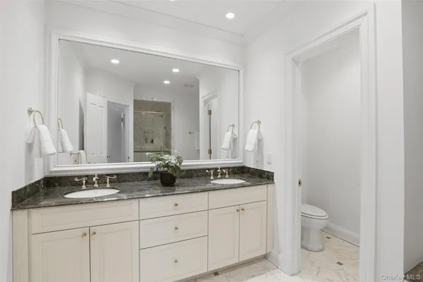 a bathroom with a granite countertop double vanity sink a mirror and a toilet