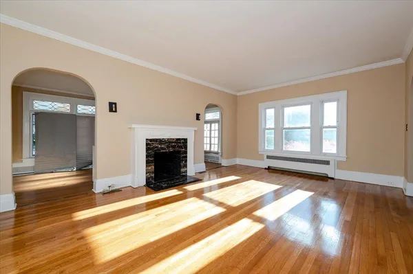 a view of an empty room with wooden floor fireplace and a window