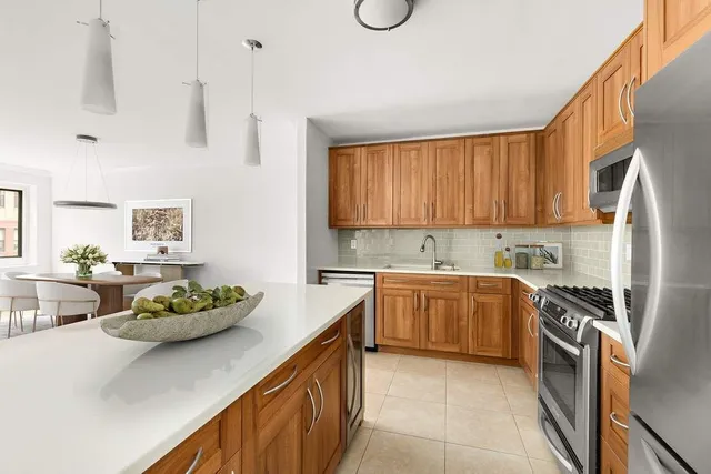 a kitchen with stainless steel appliances a stove a sink a refrigerator white cabinets and wooden floor