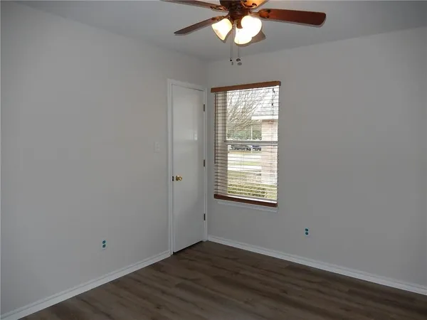 an empty room with wooden floor fan and windows
