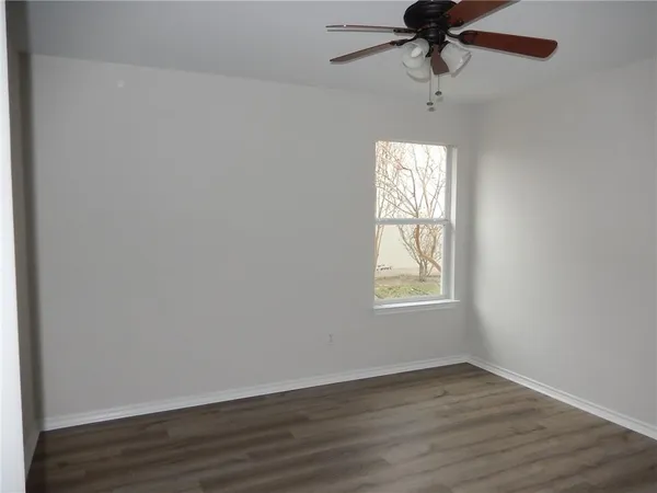 an empty room with wooden floor fan and windows
