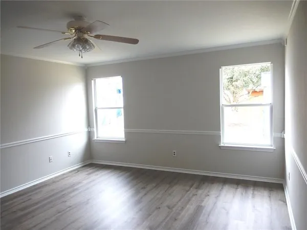 an empty room with wooden floor chandelier fan and windows