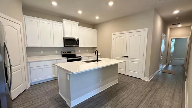 a kitchen with stainless steel appliances a stove top oven a sink a refrigerator white cabinets and wooden floor