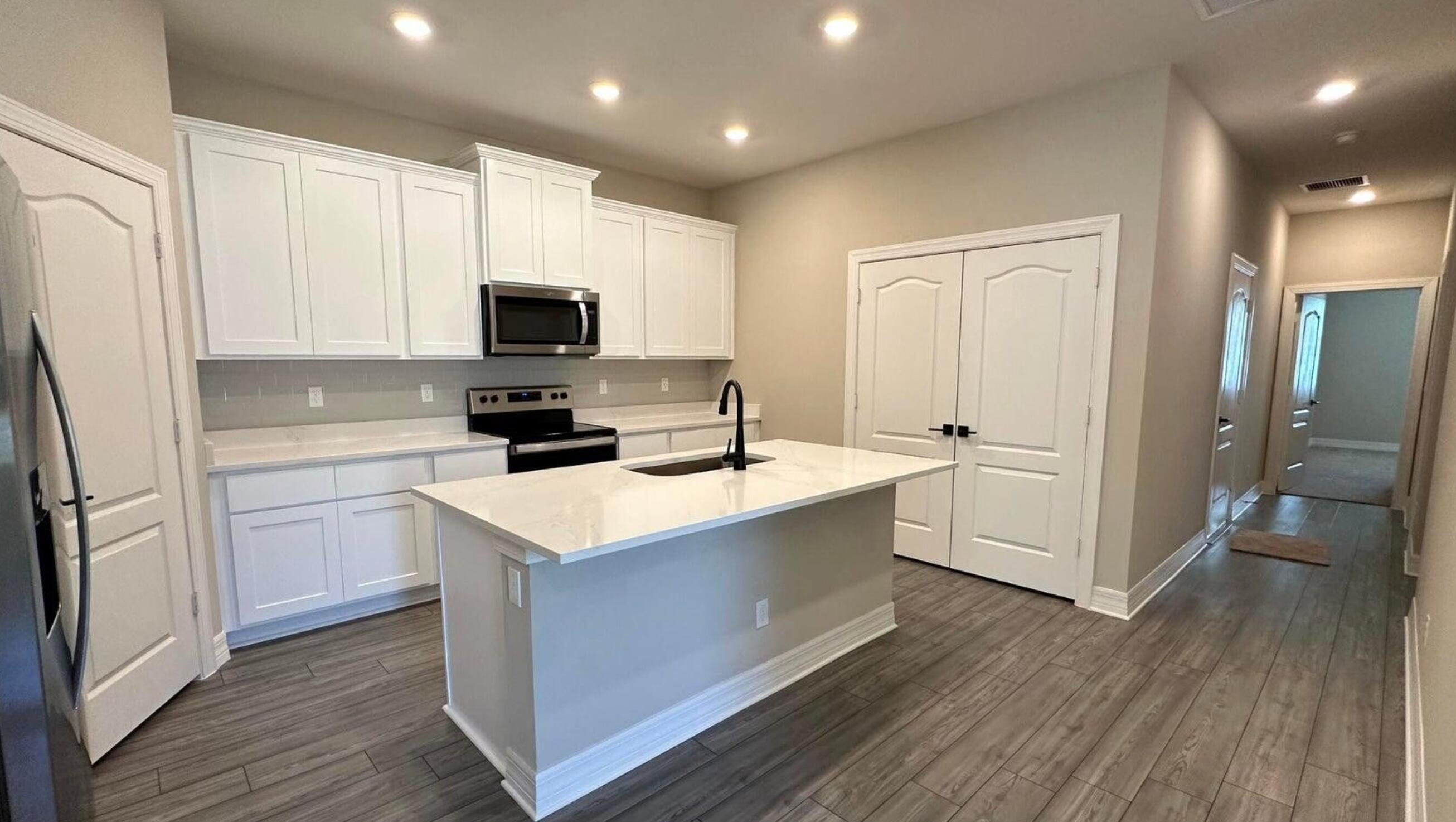 a kitchen with stainless steel appliances a stove top oven a sink a refrigerator white cabinets and wooden floor