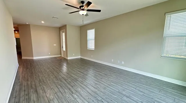 an empty room with wooden floor fan and windows