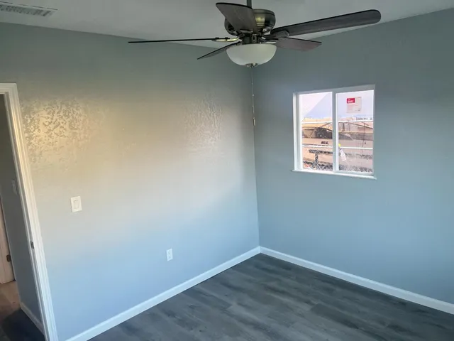 an empty room with wooden floor fan and windows