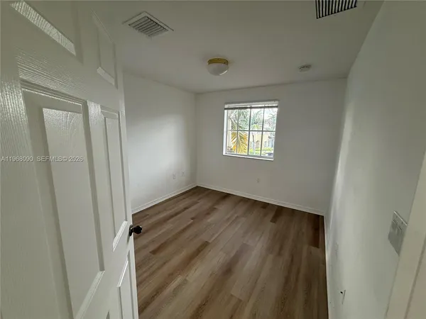 a view of an empty room with wooden floor and a window