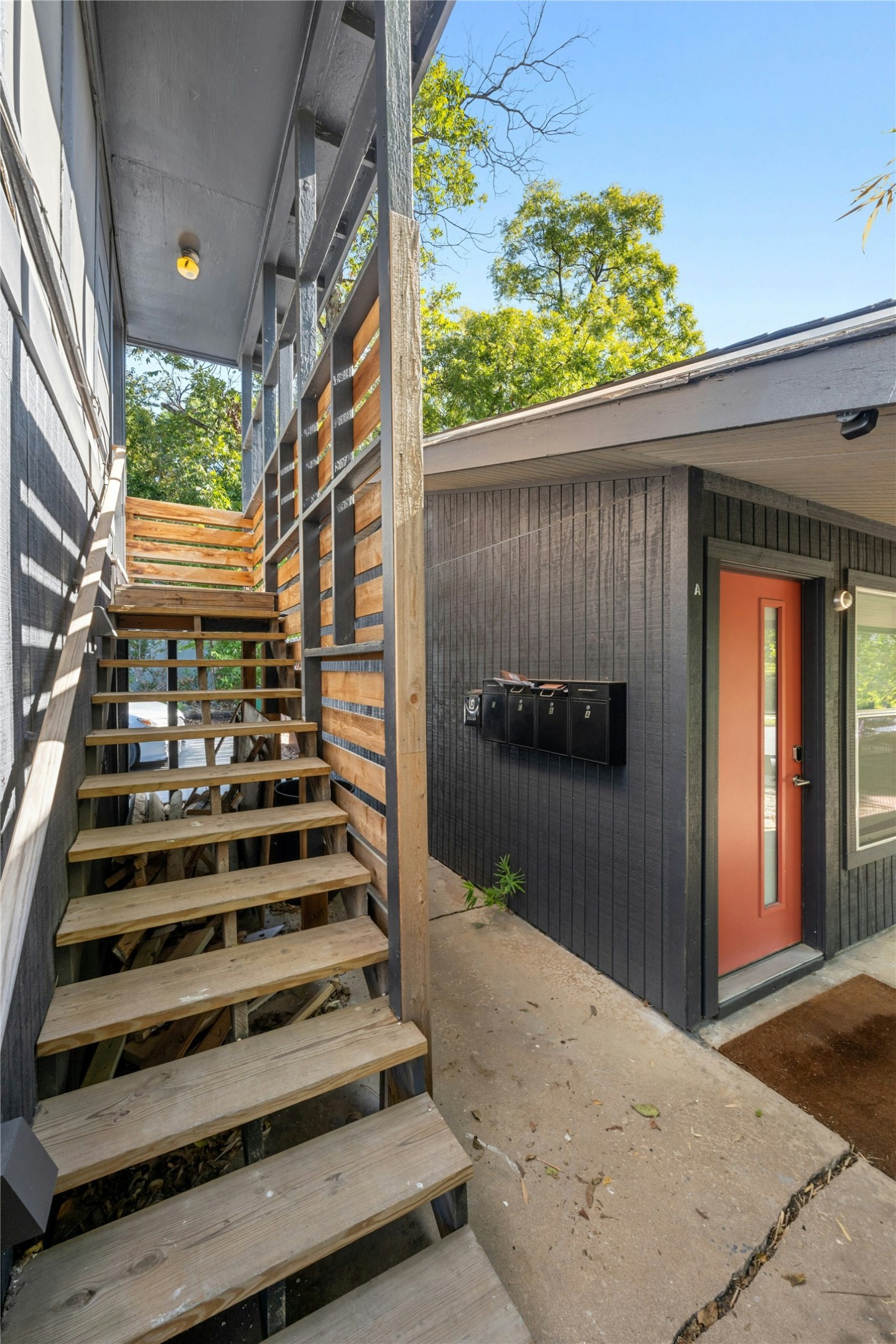 2201 Leon Street, Unit G Austin, TX 78705 - Photo 15 of 17 Exterior entryway featuring natural wood stairs, dark vertical siding, and a vibrant red entry door
