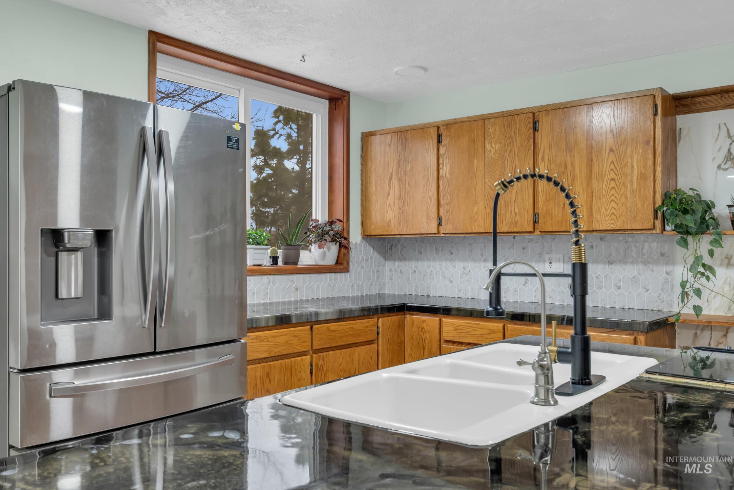 1158 South Powerline Road Nampa, ID 83686 - Photo 13 of 50 Kitchen featuring stainless steel fridge with ice dispenser, backsplash, and brown cabinets