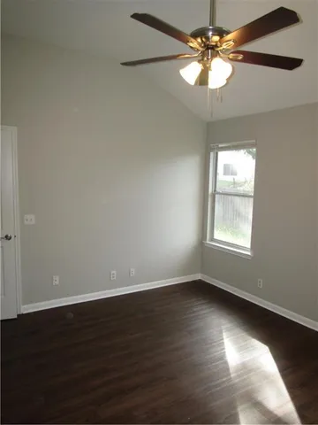 an empty room with wooden floor chandelier fan and windows