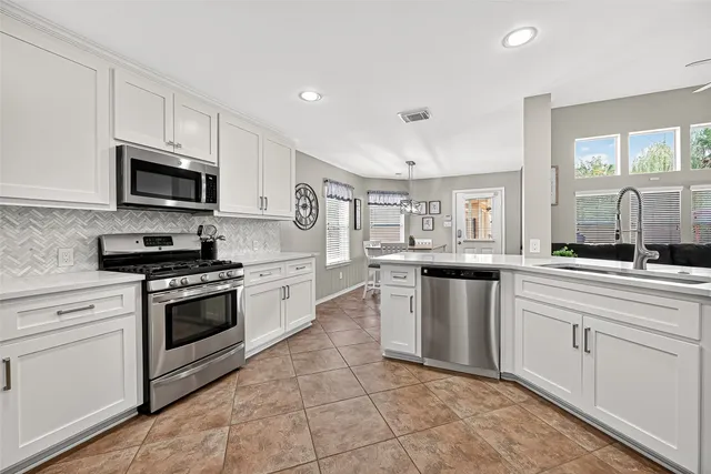 a kitchen with stainless steel appliances granite countertop a stove top oven a sink dishwasher and a microwave oven with white cabinets